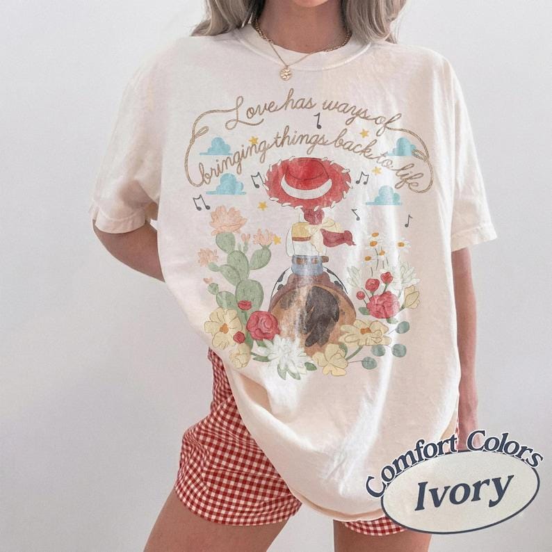 Peut inclure: Un t-shirt &agrave; manches courtes ivoire avec un motif repr&eacute;sentant une cow-girl au chapeau rouge, entour&eacute;e de cactus et de fleurs. Le texte indique, Love has ways of bringing things back to life. Le t-shirt est port&eacute; avec un short &agrave; carreaux vichy rouge.