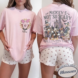 May include: Pink t-shirt and shorts set. The t-shirt features a Piglet graphic on the front and "Mickey's Not So Scary Halloween Party" on the back. The shorts are white with a small red cherry pattern. The set is labeled "Comfort Colors Blossom."