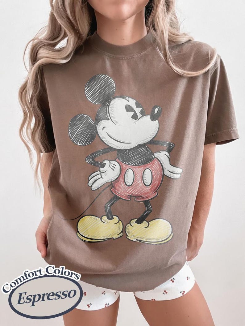 May include: Brown t-shirt featuring a sketch-style Mickey Mouse graphic. The cartoon character is in black, red, and yellow. The shirt has the words "Comfort Colors Espresso" printed on it.