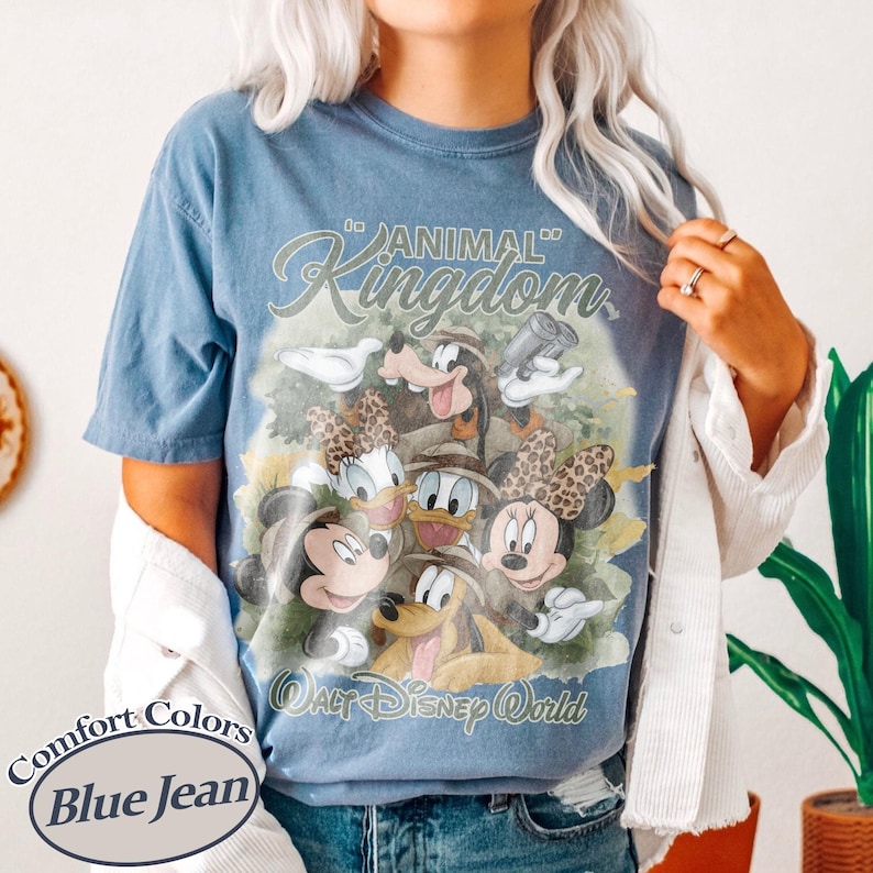 May include: Blue jean colored t-shirt featuring a graphic of Disney characters, including Mickey and Minnie Mouse, Donald and Daisy Duck, Goofy, and Pluto. The shirt has the words "Animal Kingdom" and "Walt Disney World" printed on it.