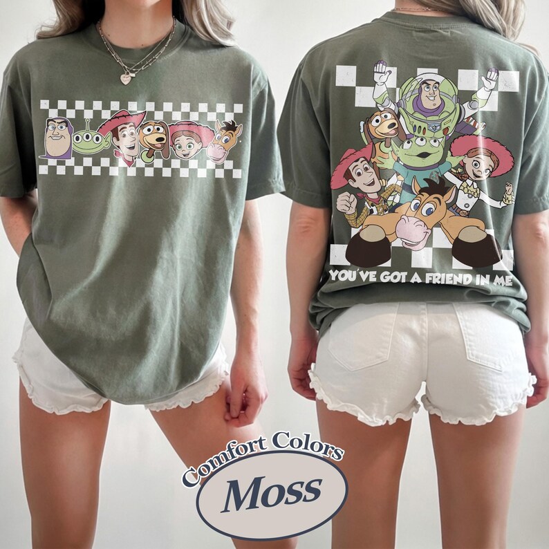 May include: Moss green t-shirt featuring a cartoon graphic of Toy Story characters on the front and back. The front graphic includes characters on a checkered background. The back graphic features the characters with the text "YOU'VE GOT A FRIEND IN ME".