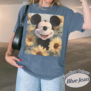 Puede incluir: Camiseta azul Comfort Colors con un gr&aacute;fico de Mickey Mouse sonriente rodeado de girasoles. La ilustraci&oacute;n tiene un estilo vintage. La camiseta tiene un corte holgado. Las palabras "Comfort Colors Blue Jean" est&aacute;n impresas en la parte inferior derecha.