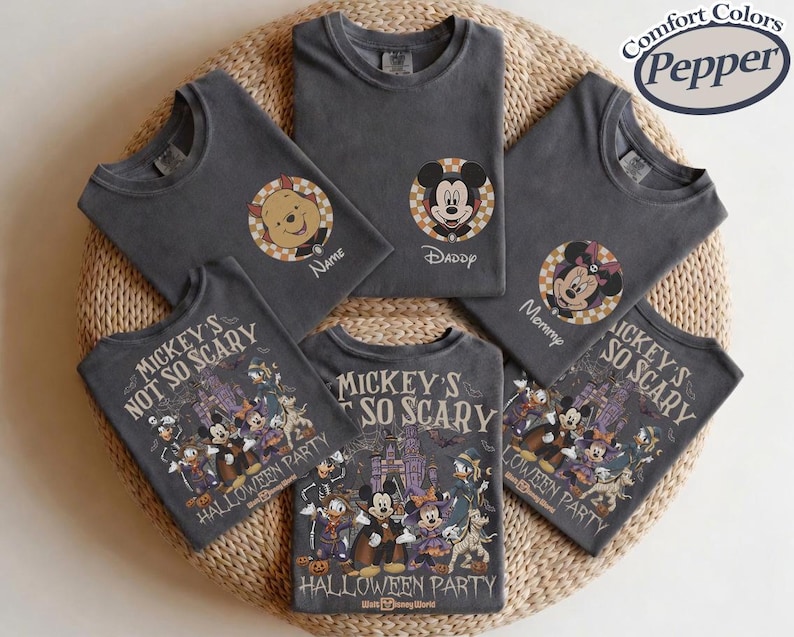 May include: Dark gray t-shirts with various Disney character designs. One shirt features Winnie the Pooh, another Mickey Mouse, and a third Minnie Mouse. Several shirts display a Halloween-themed graphic with Mickey and friends. The shirts are arranged on a woven surface.