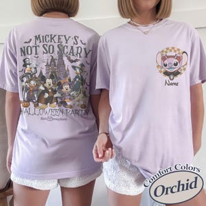 May include: Two light purple t-shirts. One features a Halloween design with Disney characters and the text "Mickey's Not So Scary Halloween Party". The other shirt has a character design with the text "Name". Both shirts are Comfort Colors brand.
