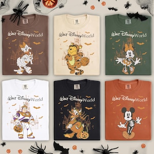 以下が含まれることがあります： ディズニーキャラクターが描かれた、ハロウィーンをテーマにしたTシャツ6枚。各シャツには「ウォルト・ディズニー・ワールド」と、ミイラ、トラ、スケルトンなど、ハロウィーンのコスチュームを着たキャラクターが描かれています。シャツの色は、茶色、白、オレンジなど様々です。