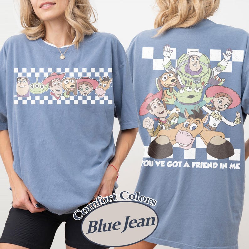 May include: Blue jean-colored t-shirt featuring characters from a popular animated film. The front displays a row of character faces above a checkered pattern. The back showcases a group of characters with the phrase "YOU'VE GOT A FRIEND IN ME".