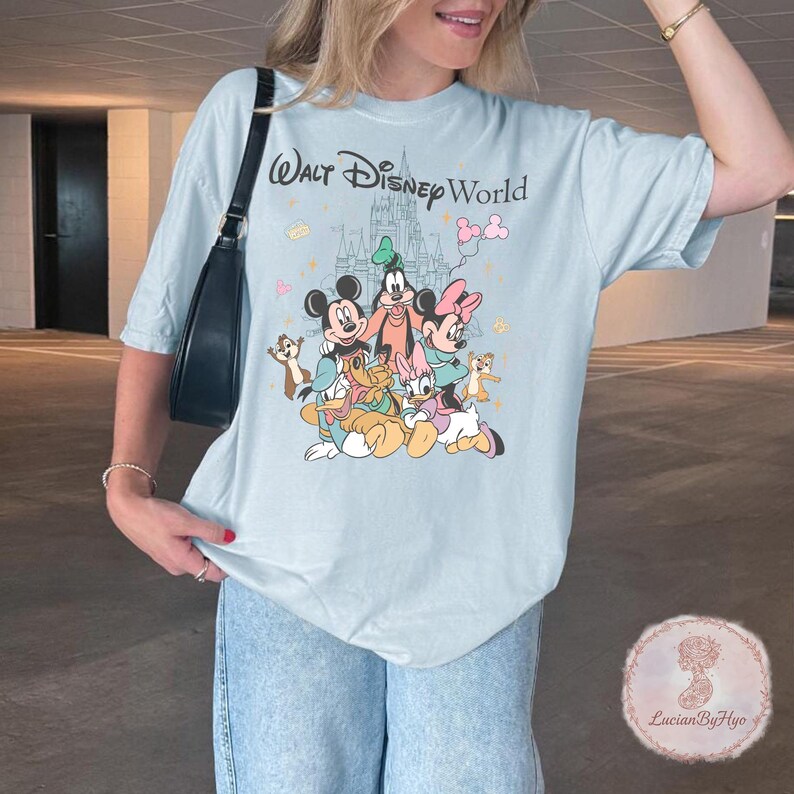 May include: Light blue t-shirt featuring the text "Walt Disney World" above a graphic of Mickey Mouse, Minnie Mouse, Goofy, Donald Duck, and other Disney characters. The shirt has a crew neck and short sleeves.