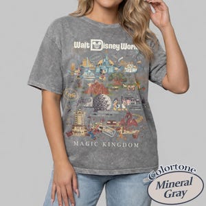 Puede incluir: Camiseta gris mineral con un gr&aacute;fico del Magic Kingdom de Walt Disney World. El dise&ntilde;o incluye ilustraciones de varias atracciones y personajes del parque, con el texto "Walt Disney World" y "Magic Kingdom".