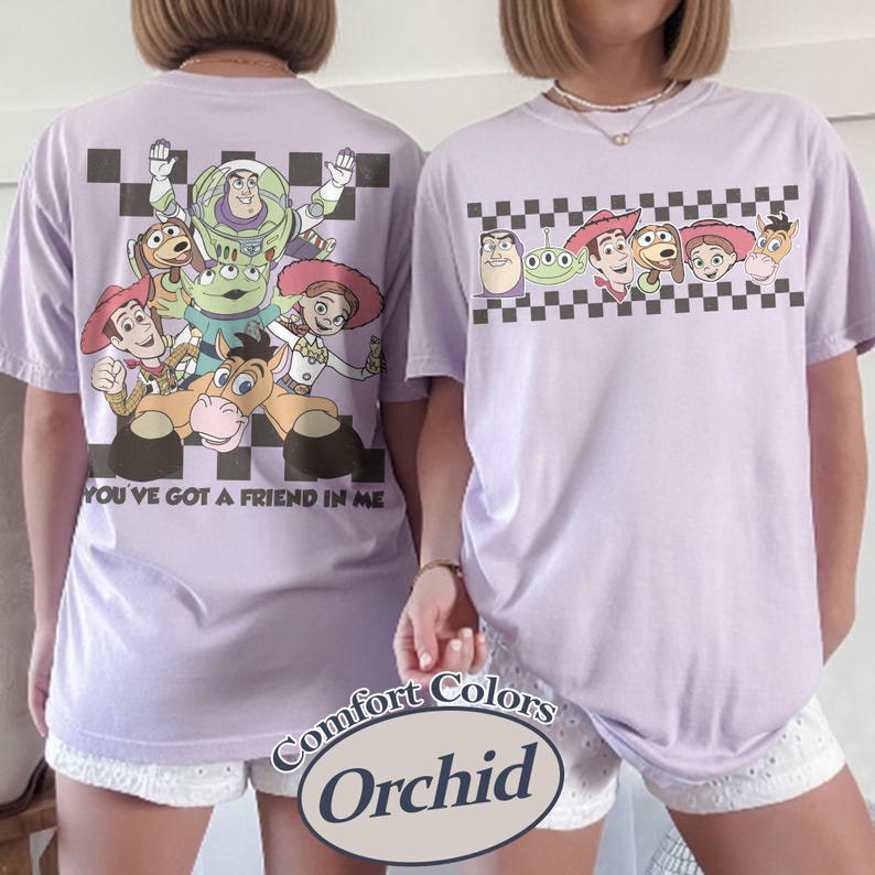 May include: Two lavender Comfort Colors t-shirts featuring Toy Story characters. One shirt has a large graphic on the back with the text "YOU'VE GOT A FRIEND IN ME." The other shirt has a smaller graphic on the front. Both shirts have a checkered pattern.