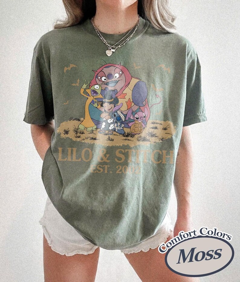 K&ouml;nnte beinhalten: Moosgr&uuml;nes T-Shirt mit einer Grafik von Lilo & Stitch-Charakteren und dem Text "Lilo & Stitch EST. 2002". Das Shirt ist von der Marke Comfort Colors.