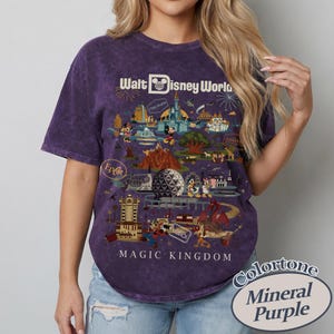 Puede incluir: Camiseta morada con un gr&aacute;fico de Walt Disney World que presenta varias atracciones y personajes del parque. La camiseta incluye el texto "Magic Kingdom" y "Epcot". La camiseta es morada mineral.