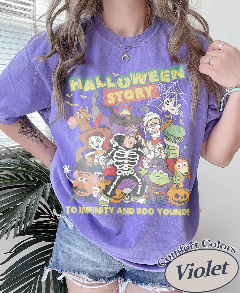 May include: Violet Comfort Colors t-shirt with a Halloween Story graphic featuring cartoon characters. The design includes the text "TO INFINITY AND BOO YOUND!" and a spiderweb. The shirt is a crew neck.