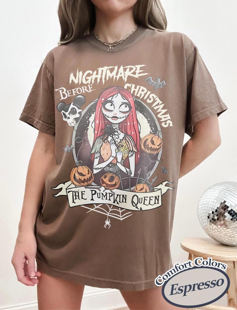 Puede incluir: Camiseta marr&oacute;n con un dise&ntilde;o gr&aacute;fico de "Pesadilla antes de Navidad". El dise&ntilde;o incluye a Sally, calabazas y el texto "The Pumpkin Queen". La camiseta est&aacute; etiquetada como "Comfort Colors Espresso".