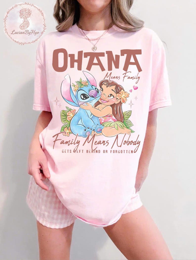 May include: Pink t-shirt featuring a graphic of Stitch and Lilo from Lilo & Stitch, with the words "Ohana Means Family" and "Family Means Nobody Gets Left Behind or Forgotten". The design includes floral accents and hearts.
