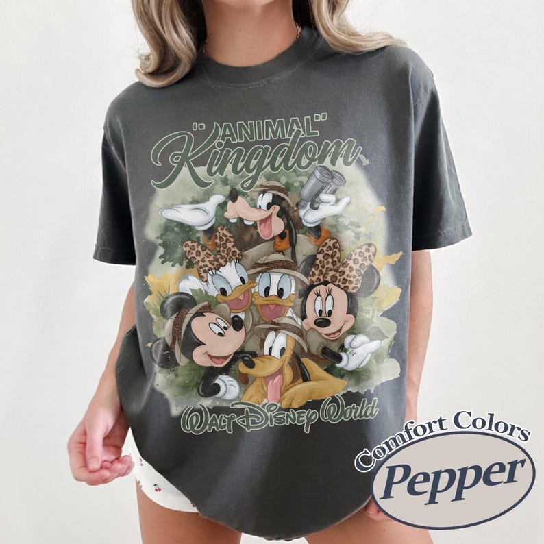 May include: Dark gray t-shirt featuring a graphic of Disney characters, including Mickey and Minnie Mouse, Donald and Daisy Duck, Goofy, and Pluto, with the text "Animal Kingdom" and "Walt Disney World". The shirt is labeled "Comfort Colors Pepper".