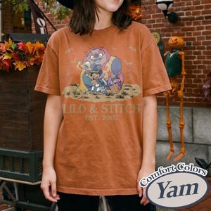 K&ouml;nnte beinhalten: Gebrannt orangefarbenes T-Shirt mit einer Grafik von Lilo & Stitch-Charakteren und dem Text "LILO & STITCH EST. 2002". Das Shirt ist von der Marke Comfort Colors, mit einem Yam-Farbetikett.