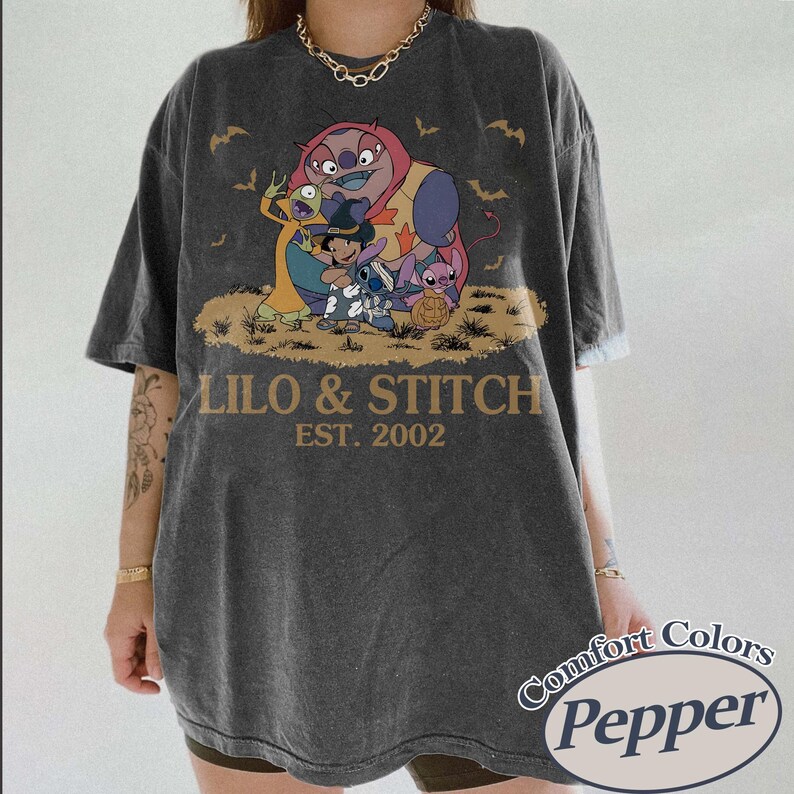 K&ouml;nnte beinhalten: Dunkelgraues T-Shirt mit einer Grafik von Lilo & Stitch-Charakteren und dem Text "Lilo & Stitch EST. 2002." Das Shirt hat einen Vintage-Look und das Comfort Colors Pepper-Logo.