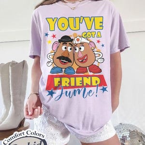 Op de afbeelding: Een lichtpaars T-shirt met de tekst "YOU'VE GOT A FRIEND Jume!" en een afbeelding van twee aardappelvormige personages. Het shirt is van het merk Comfort Colors in de kleur Orchid.