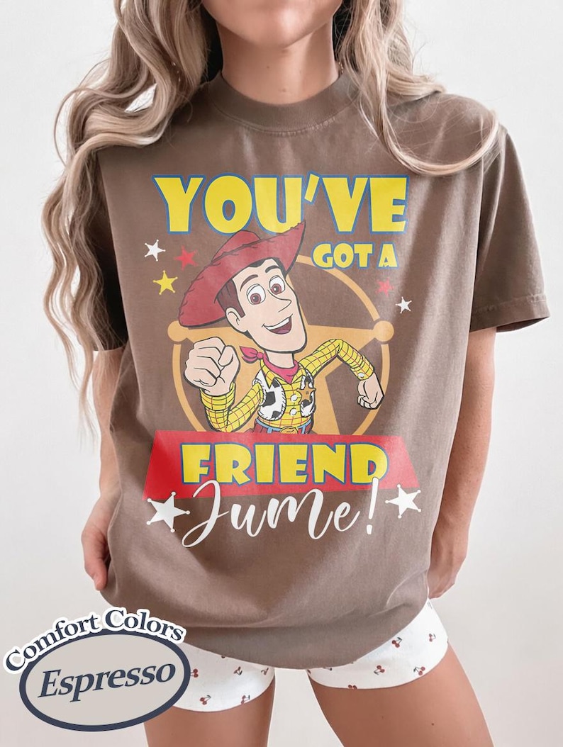 Op de afbeelding: Espresso-kleurig T-shirt met een Woody uit Toy Story-afbeelding. Het ontwerp bevat de tekst "YOU'VE GOT A FRIEND Jume!" in geel en wit, met sterren en een rode banner. Het shirt is van Comfort Colors.