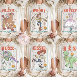 May include: Cream-colored t-shirts featuring cartoon characters from the movie Toy Story. Each shirt displays a different character: Bullseye, Woody, Bo Peep, Buzz, Jessie, and Rex, with the text "You've Got a Friend in Me" and "Est. 1997".