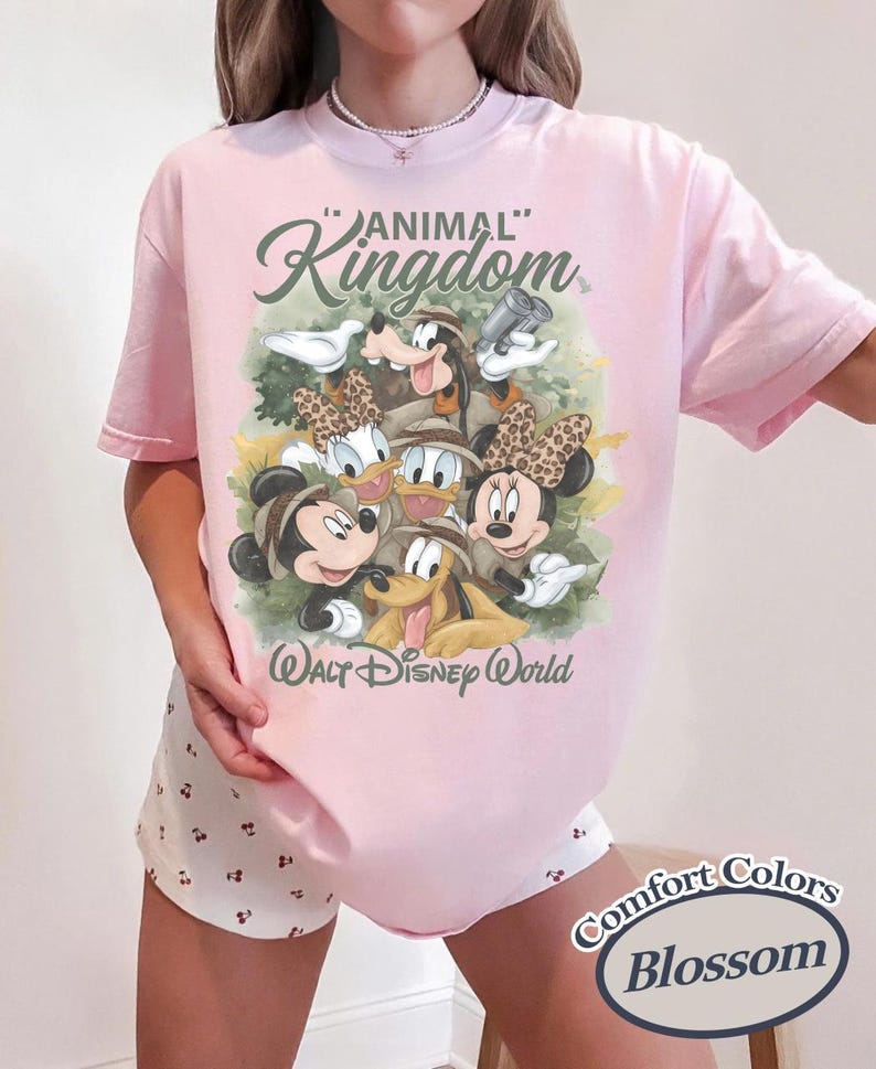 May include: A light pink t-shirt featuring a graphic of Disney characters, including Mickey and Minnie Mouse, Donald and Daisy Duck, and Goofy. The shirt has the words "Animal Kingdom" and "Walt Disney World" printed on it.