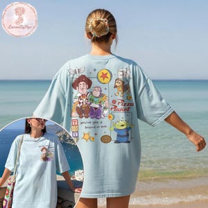 Puede incluir: Camiseta azul claro con los personajes de dibujos animados Woody, Buzz Lightyear y otros de Toy Story. La camiseta tiene el texto "You've got a friend in me" y "Pizza Planet".