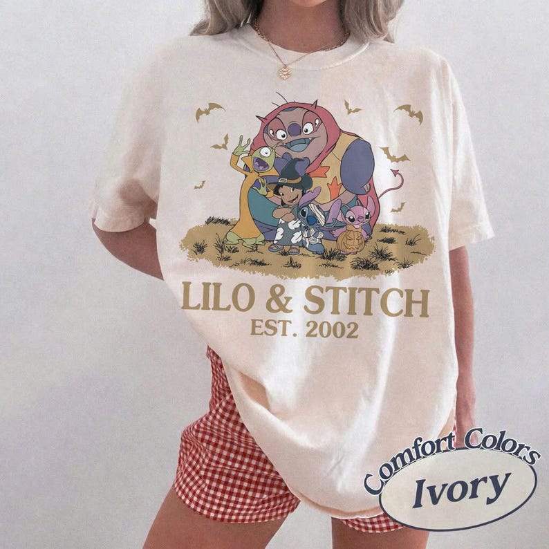 K&ouml;nnte beinhalten: Cremefarbenes T-Shirt mit einem Halloween-Motiv von Lilo & Stitch. Unter der Illustration steht der Text "LILO & STITCH EST. 2002". Das Shirt ist von der Marke Comfort Colors.