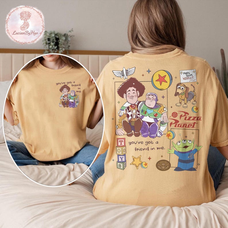 Puede incluir: Camiseta de color mostaza con un gr&aacute;fico de Woody y Buzz Lightyear con el texto "you've got a friend in me". La parte posterior de la camiseta muestra personajes y texto adicionales de Toy Story. Una camiseta divertida e informal.