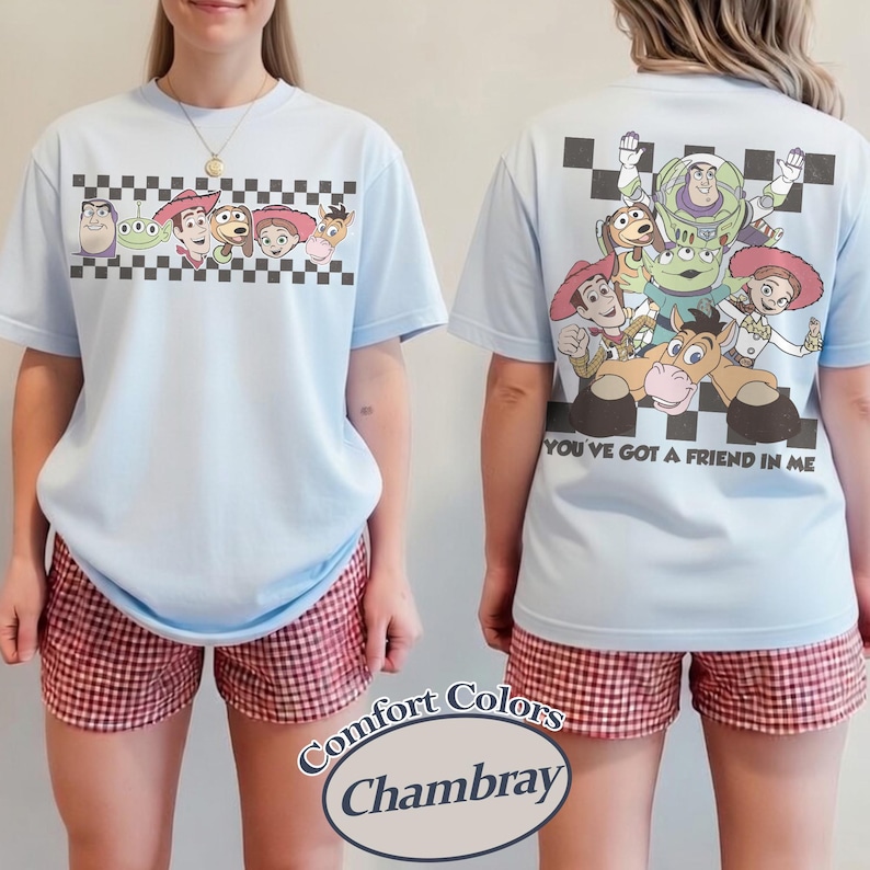 May include: Light blue t-shirt featuring Toy Story characters on the front and back. The front has a checkered border with characters, and the back displays a group of characters with the text "YOU'VE GOT A FRIEND IN ME". The shorts are red and white checkered.