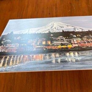 May include: A painting of a city skyline with a snow-capped mountain in the background. The city is lit up with lights, and the water in the foreground reflects the lights.