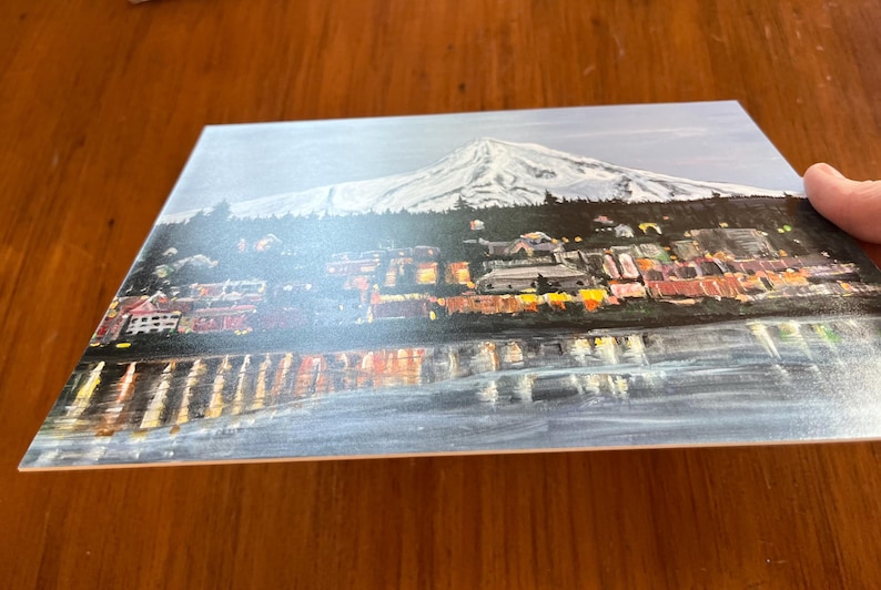 May include: A painting of a city skyline with a snow-capped mountain in the background. The city is lit up with lights, and the water in the foreground reflects the lights.