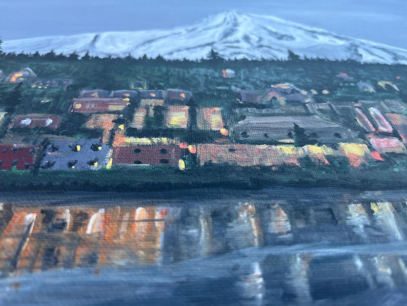 May include: A painting of a snowy mountain peak with a small town at the base. The town is lit up with warm yellow lights, and the water in the foreground reflects the lights.