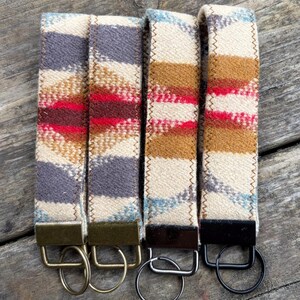 May include: Four key fobs with colorful woven fabric straps. The straps feature a pattern of cream, red, brown, blue, and gray stripes. Each fob has a metal ring and a metal clasp in various colors.