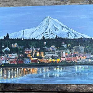 May include: A painting of a snow-capped mountain with a town in the foreground. The town is lit up with lights and there is a body of water in front of it. The sky is a light blue color.