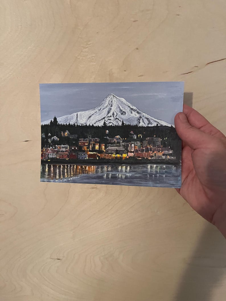 May include: A painting of a snow-capped mountain with a city in the foreground. The city is lit up with lights, and the mountain is reflected in the water in the foreground.