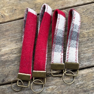 May include: Four key fobs with fabric straps in red and gray plaid patterns. The key fobs have brass-colored metal hardware and key rings. The fabric is stitched with white thread.