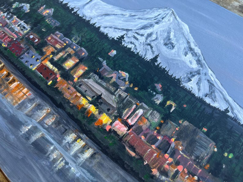 May include: A painting of a snowy mountain range with a town at the base. The town is lit up with warm, yellow lights. The sky is a soft blue.