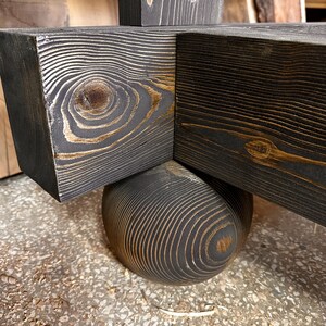 May include: Close-up of a wooden structure with a dark gray stain, showcasing the natural wood grain. The design features intersecting beams and a rounded base, highlighting the craftsmanship and texture of the wood.