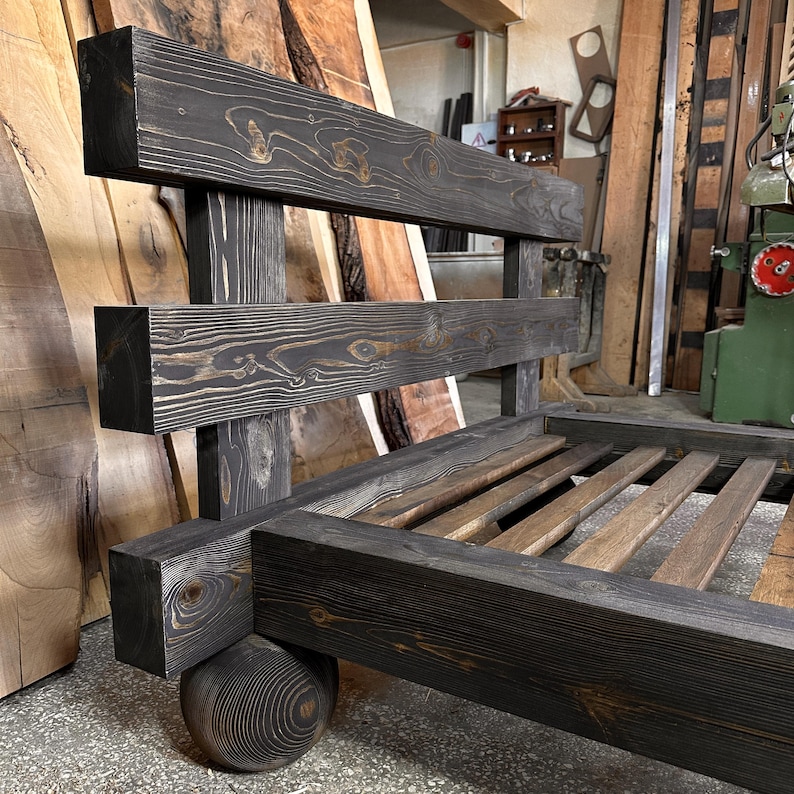 May include: A handcrafted, dark-stained wooden bed frame with a unique design. The headboard features horizontal beams, and the bed rests on a spherical wooden base. The frame's construction showcases visible wood grain, adding to its rustic charm. The bed frame is a statement piece.