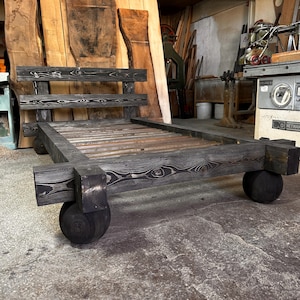 May include: A handcrafted, dark-stained wooden bed frame with a headboard and a slatted base. The bed frame is supported by four large, rounded wooden feet. The wood grain is visible throughout the frame, adding to its rustic charm. The bed frame measures approximately 78 inches long.