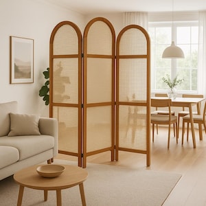 May include: A wooden three-panel room divider with woven cane inserts. The arched top design adds a touch of elegance. The divider is in a living room setting with a sofa, coffee table, and dining area visible.