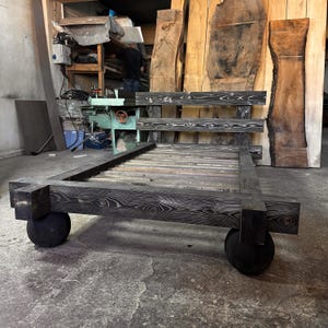 May include: A low-profile, dark-stained wooden bed frame with a headboard and footboard. The frame rests on four large, black, spherical feet. The wood grain is visible, and the design is minimalist and modern.