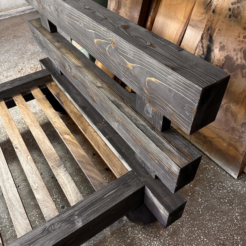 May include: A dark gray wooden bed frame with a slatted base. The headboard and footboard are constructed from thick, square timbers, showcasing the natural wood grain. The bed frame is designed with a modern, minimalist aesthetic.