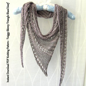 May include: A delicate, grey knitted triangle shawl with a lacy pattern. The shawl is draped over a blue hanger.