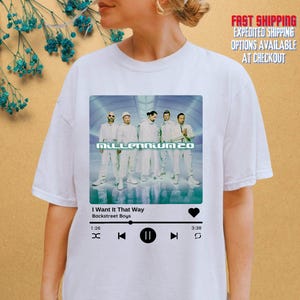 May include: White t-shirt featuring a graphic of the Backstreet Boys album "Millennium 2.0" with the song "I Want It That Way." The design includes a music player interface with play, pause, and skip controls.