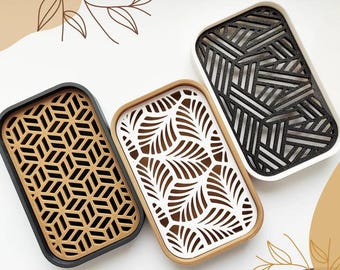 May include: Three rectangular soap dishes with removable inserts. One has a black frame with a tan geometric pattern, one has a tan frame with a white leaf pattern, and one has a white frame with a black linear pattern.