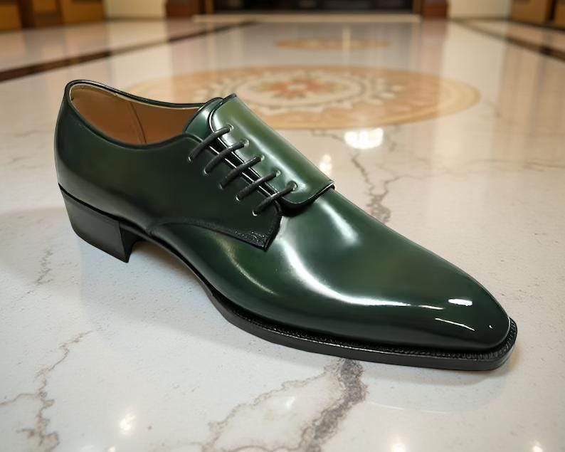 May include: A single, glossy, dark green leather dress shoe with black laces. The shoe has a square toe and a low heel. The shoe is sitting on a marble surface.
