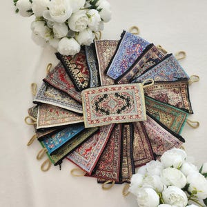 Könnte beinhalten: Eine Ansammlung rechteckiger Reißverschlusstaschen, die kreisförmig angeordnet sind und jeweils komplexe Webmuster aufweisen, die an traditionelle Teppichdesigns in verschiedenen Farben wie Rot, Blau, Grün und Schwarz erinnern, mit goldenen Reißverschlussanhängern.