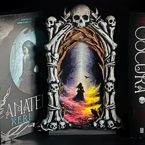 May include: A decorative, gothic-style archway with a skull at the top and smaller skulls along the sides. The archway frames a colorful painting of a silhouetted figure in a dark landscape. Flanking the arch are two books with titles in Spanish.