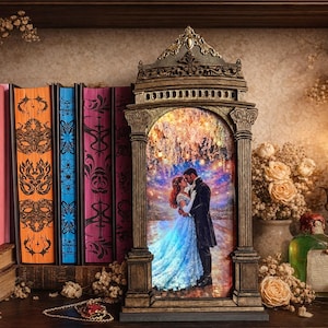 Puede incluir: Un marco de fotos ornamentado de estilo antiguo con una escena romántica de una pareja abrazándose. El marco está colocado en una estantería con libros y una vela encendida. La escena está iluminada con una luz cálida, creando un ambiente acogedor e invitador.